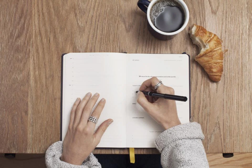 Content writer drafting article ideas in a notebook beside a coffee